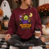 Close-up of a woman sitting outside holding a coffee cup, wearing a cozy maroon crewneck sweatshirt customized with a colorful spooky season digital Halloween sublimation PNG.
