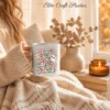 Cozy fall scene of a person wrapped in a cream knit blanket, holding a white ceramic coffee mug printed with a cute ghost Hocus Pocus I Need Candy to Focus PNG design next to a lit candle.