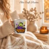 Close-up of a person wrapped in a cozy, cream-colored knit blanket holding a white ceramic sublimation mug printed with a cute green Frankenstein Monster Munch Halloween design by a sunny window.