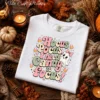 Flat lay white crewneck sweatshirt with Halloween sublimation design, surrounded by cozy knitted blankets, pinecones, autumn leaves, and glowing candles.