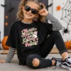 oung girl with pigtails wearing sunglasses and a black layered long-sleeve t-shirt with retro Halloween clipart design printed on the front.