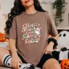 Woman wearing a brown cotton t-shirt with cute Halloween art sublimation print, sitting on the floor with plush ghosts and a pumpkin candy bucket.