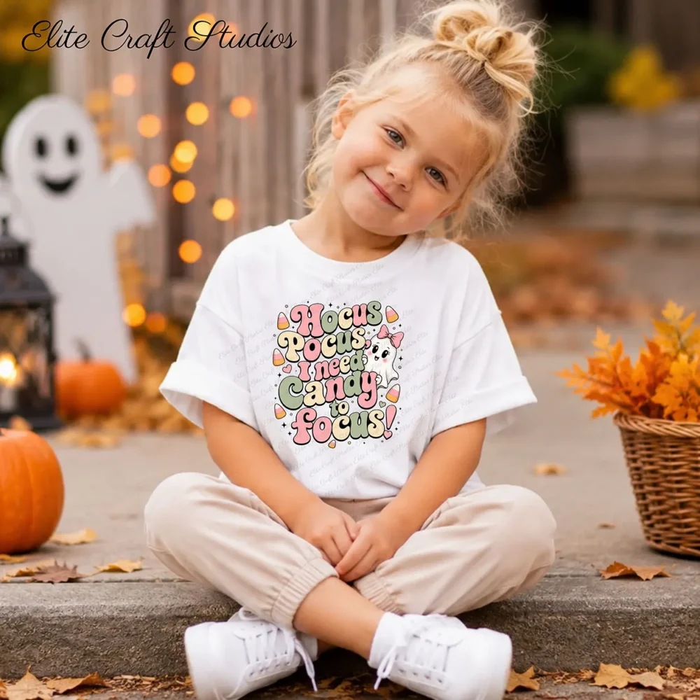 Smiling little girl sitting on outdoor concrete steps in a white t-shirt printed with fall sublimation PNG art, surrounded by fall leaves and a ghost prop.