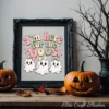 A dark ornate picture frame displays the cute coquette ghost bow PNG print, set on a rustic wooden table flanked by carved jack-o'-lantern pumpkins and a black twig tree.