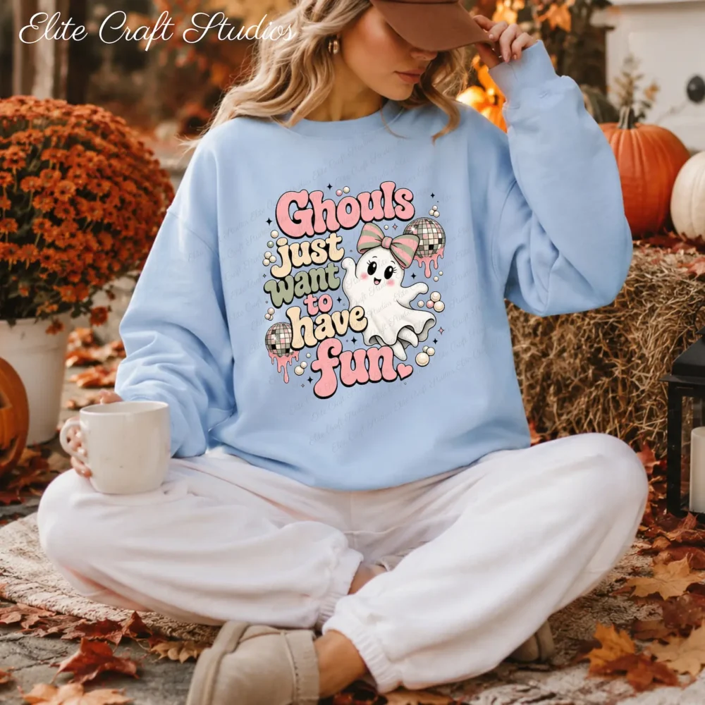 Model sitting outside among autumn leaves wearing a light blue crewneck sweatshirt with the retro pink ghost graphic.