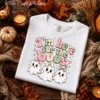 Folded white Comfort Colors sweatshirt displaying the retro here for the boos png design in an autumn flat lay.