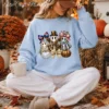 Woman sitting outside against hay bales wearing a light blue oversized sweatshirt with a steampunk ghost PNG sublimation design.