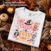 Creepy and Cute Halloween PNG design printed on a folded white Comfort Colors t-shirt surrounded by autumn leaves, candles, and pinecones.