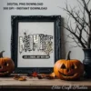 Ornate black picture frame displaying the Mombie art print positioned between two carved pumpkins on a wooden tabletop.