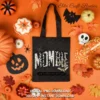 Flat lay of an orange background with a black tote bag featuring the Mombie graphic surrounded by Halloween candy and pumpkins.