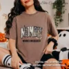 Woman sitting in a cozy room wearing a brown t-shirt featuring the distressed leopard Mombie design.