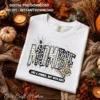 Flat lay of a white t-shirt printed with the Mombie Halloween graphic surrounded by pinecones, fall leaves, and a lit candle.