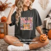 Model sitting cross-legged wearing a washed charcoal t-shirt featuring the Creepy and Cute sublimation design while holding an orange pumpkin mug.