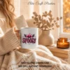 Close-up of a woman in a knit blanket holding a white ceramic coffee mug printed with the pink spooky cowgirl design.