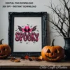 Black ornate picture frame holding the pink spooky cowgirl art print on a wooden mantel flanked by carved jack-o'-lanterns.