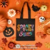Flat lay view of a black tote bag printed with the Spooky Season design, surrounded by scattered autumn leaves, miniature pumpkins, and candy corn.