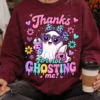 Woman wearing a maroon crewneck sweatshirt with the ghost graphic printed on the chest while holding a to-go coffee cup.