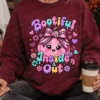 Model wearing a cozy maroon crewneck sweatshirt with the Bootiful Inside and Out pink pumpkin design, holding a to-go coffee cup.