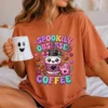 Model in an oversized terracotta t-shirt printed with the pastel spooky coffee illustration, holding a white ceramic ghost coffee mug.