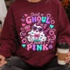 Woman holding a takeaway coffee cup while wearing a maroon crewneck sweatshirt with the Just a Ghoul Who Loves Pink ghost print.