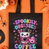 Black tote bag printed with the kawaii Spookily Obsessed with Coffee artwork laid flat on a bright orange background with Halloween decor.