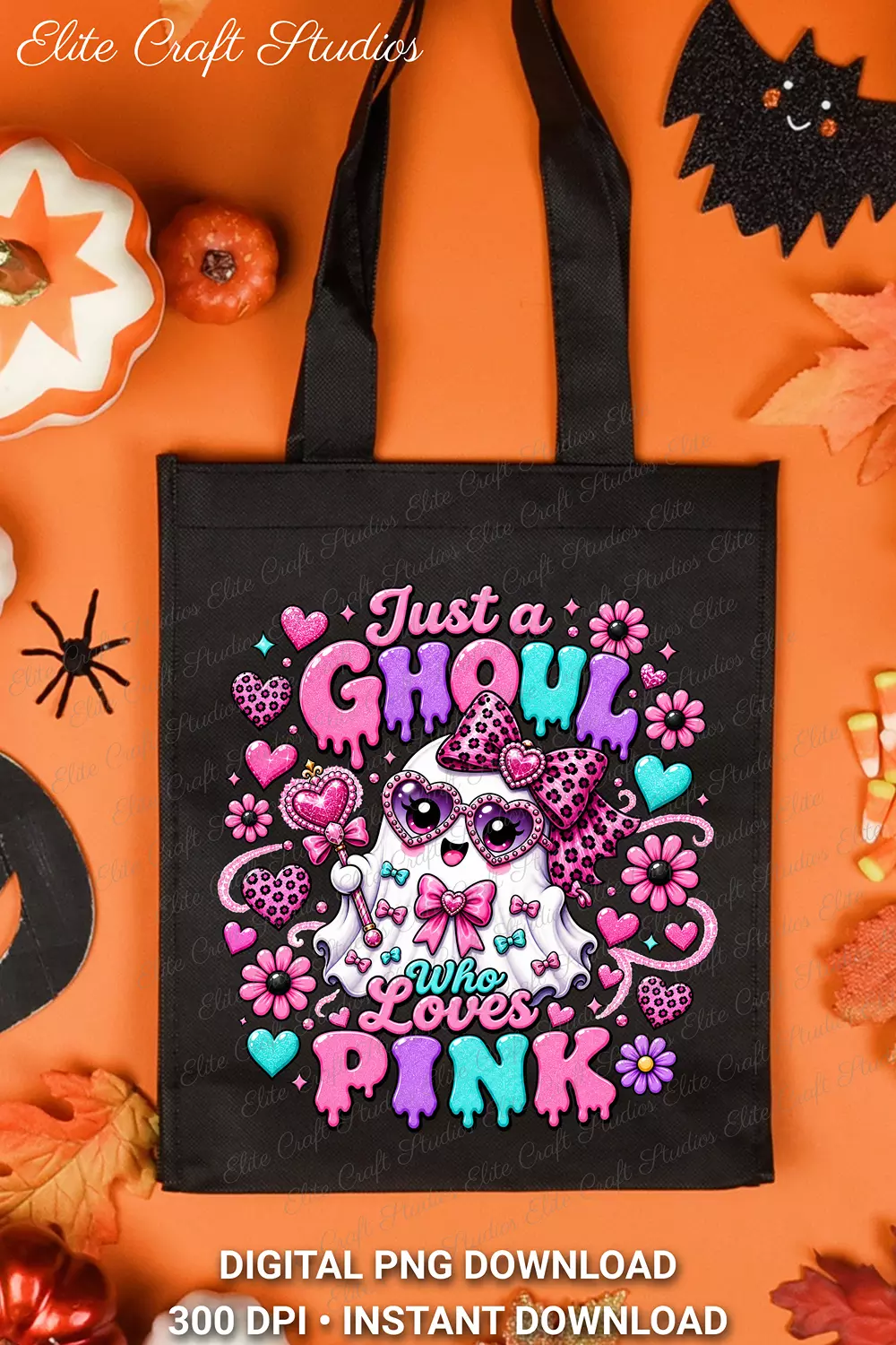 Black canvas tote bag printed with the Just a Ghoul Who Loves Pink design, laid flat on an orange surface with Halloween decor, autumn leaves, and candy corn.