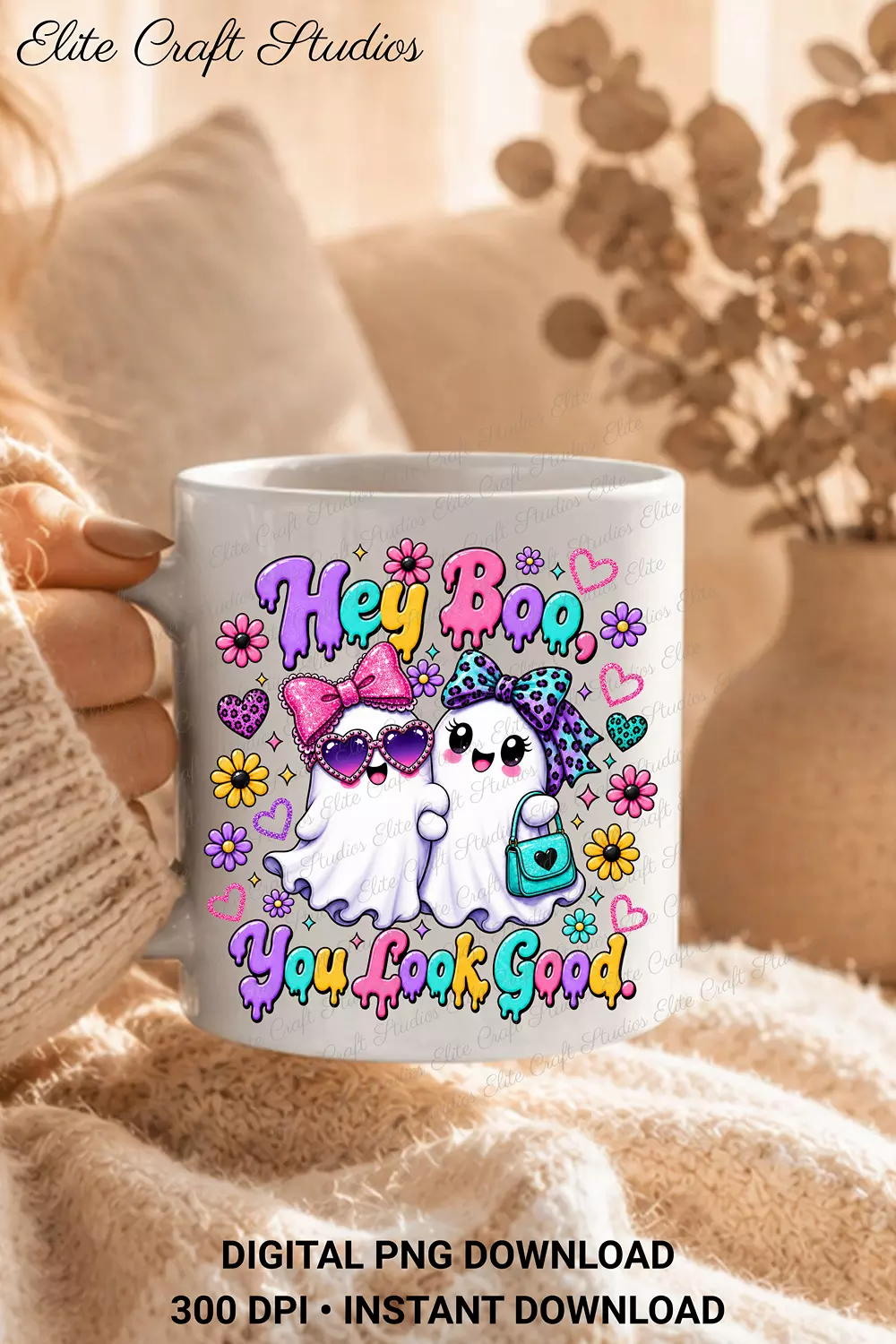 Hand holding a white ceramic mug printed with the colorful Hey Boo ghost design against a soft knit blanket background.