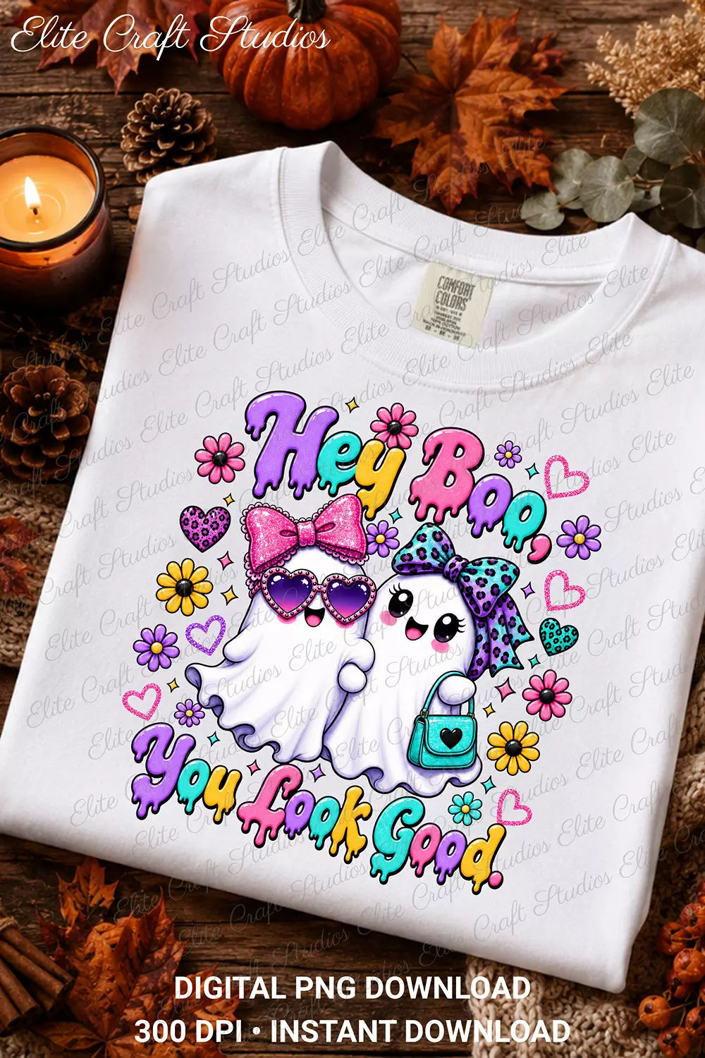 Folded white crewneck shirt displaying the Hey Boo You Look Good ghost graphic surrounded by autumn leaves, pinecones, and a lit candle.