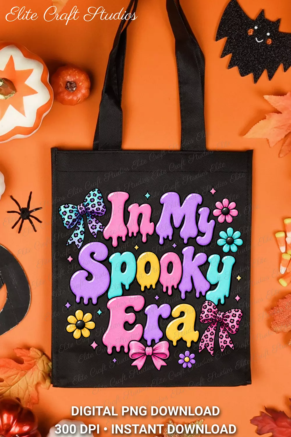 Flat lay of a black canvas tote bag printed with the In My Spooky Era design on an orange backdrop surrounded by Halloween decor, candy corn, and fall leaves.