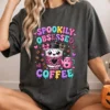 Smiling woman wearing a washed charcoal graphic t-shirt with the Spookily Obsessed with Coffee design, holding a small orange pumpkin.