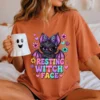 Woman sitting in an orange t-shirt featuring the resting witch face bat print while holding a ghost mug.