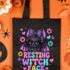 Black reusable tote bag featuring the resting witch face bat design flat-layed on orange background with fall decor.