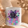 Hand holding a white glossy ceramic mug printed with the resting witch face bat artwork against a cozy blanket.