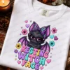 Folded white graphic t-shirt with resting witch face bat design placed among fall leaves, pinecones, and candle.