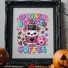 Framed Spookily Obsessed with Coffee art print displayed in a decorative black frame on a wooden table flanked by carved Halloween pumpkins.