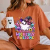 Woman sitting in a cozy bedroom setting wearing a terracotta orange crewneck t-shirt featuring the Feeling Wickedly Awesome ghost graphic while holding a white ceramic ghost face mug.